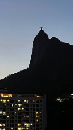 a tall building with a cross on top in front of a large mountain at night