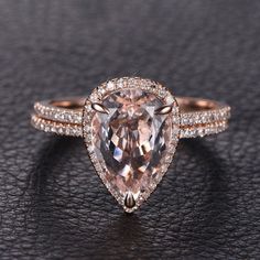 an engagement ring with a pear shaped morganite surrounded by pave diamonds on a black surface