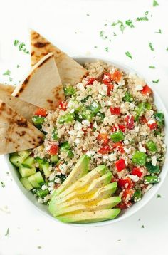 a white bowl filled with rice, cucumber and other vegetables next to tortilla wedges