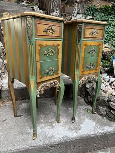 two green and gold painted nightstands sitting next to each other on the cement ground