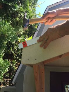 a person is holding a hammer over a piece of wood on top of a house