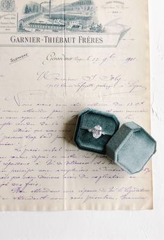 an open ring box sitting on top of a piece of paper with writing underneath it