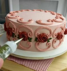 someone is decorating a cake with pink frosting and roses on it, while the icing is being applied