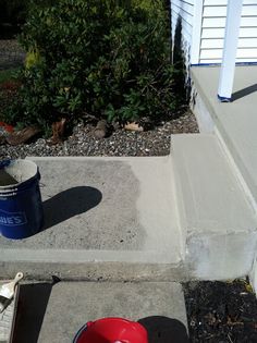 a red bucket sitting on the side of a cement step next to a blue bucket