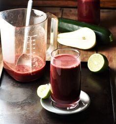 a pitcher and glass filled with liquid on top of a tray next to cucumbers