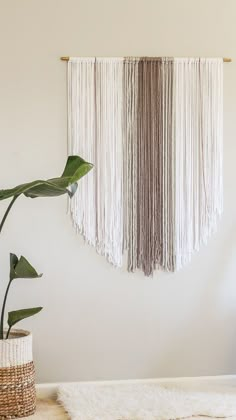 a white wall hanging in a living room next to a potted plant