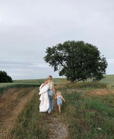 a woman and child walking down a dirt path in the middle of an open field