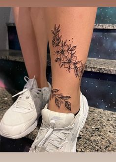 a woman's leg with a flower tattoo on her left ankle and white sneakers