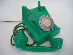 an old fashioned green phone is sitting on the table next to it's cord