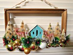 a frame with ornaments hanging from it's sides and a house in the middle