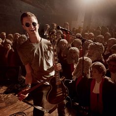 a man holding a guitar standing in front of a group of people