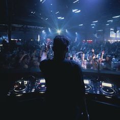 a dj in front of a large crowd at a music concert with his hands up