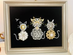 three brooches are displayed in a frame on a table next to a vase