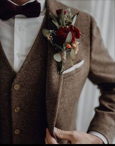 a man in a brown suit and bow tie is holding his jacket over his chest