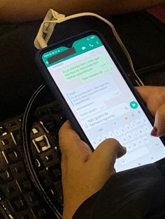 a person is using their cell phone while sitting on a bench in front of a keyboard