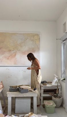 a woman standing in front of a painting on a easel next to a table