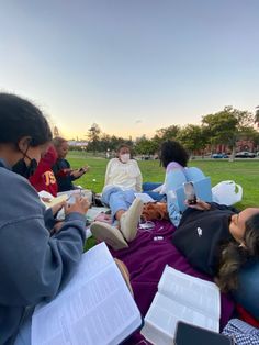 several people are sitting on the grass with books and notebooks in their hands as they look at something