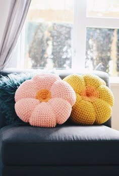 two knitted pillows sitting on top of a black couch next to a large window