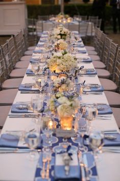 a long table is set up with blue and white linens, silverware, and flowers