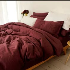 a bed with red sheets and pillows in a white room next to a small table