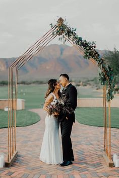 a bride and groom kissing under an arch with greenery at their wedding in the desert