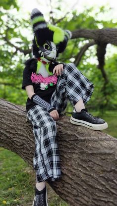 a person sitting on top of a tree branch wearing a mask and checkered pants