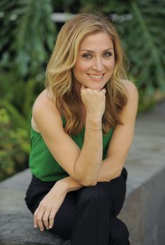 a woman is sitting on a ledge with her hand under her chin and looking at the camera