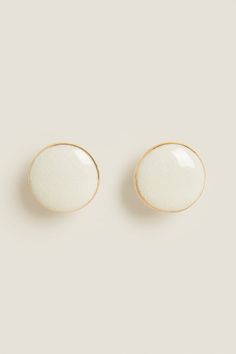 two white earrings with gold trims on each ear, one in the shape of an oval