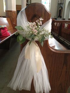 a bouquet of flowers is tied to the back of a church pew with white tulle