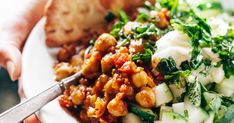 a person is holding a fork over a plate of food with bread and greens on it