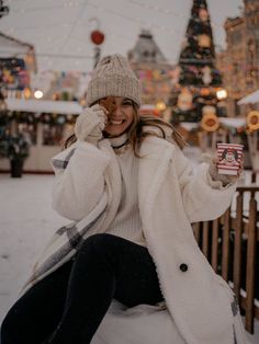 a woman is sitting in the snow with her cell phone up to her ear and smiling