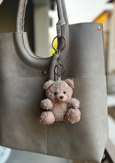 a teddy bear keychain hanging from a gray purse with a chain attached to it