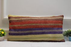 a colorful striped pillow sitting on top of a white floor next to potted plants