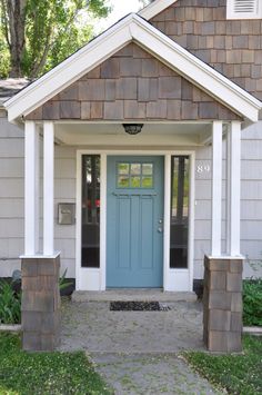 a blue door sits in front of a gray house with white trim and columns on the side