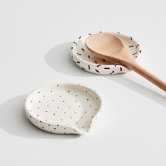 two bowls and a wooden spoon on a white surface with black dots, one has a wood spoon in the shape of a bowl