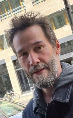 a man with a goatee and beard standing in front of a building on a city street