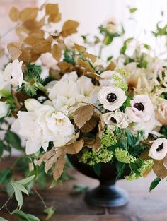 a vase filled with lots of white flowers on top of a wooden table covered in greenery