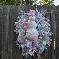 a snowman wreath is hanging on a wooden fence with ornaments around it and in the center