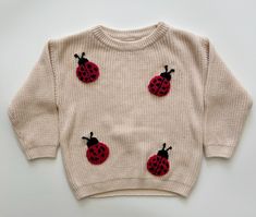 a sweater with red and black ladybugs on the front, sitting on a white surface