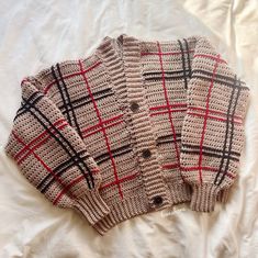 a sweater that is laying on top of a white sheet with a black and red checkered pattern