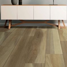 a white sideboard sitting on top of a wooden floor next to a vase filled with flowers