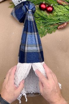 someone is making a christmas ornament out of yarn and fabric, with pine branches in the background