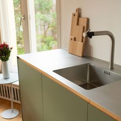 a kitchen sink sitting under a window next to a vase with flowers in it and a cutting board on the counter