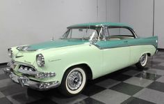 an old green and white car is parked in a room with checkered flooring