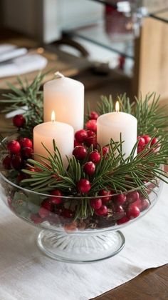 three candles are lit in a glass bowl filled with holly berries and pine cones on a table