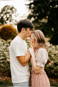 a man and woman standing next to each other in front of some bushes with flowers