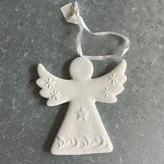 a ceramic angel ornament hanging from a white ribbon on a gray table top