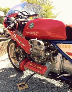 a red motorcycle parked on top of a gravel covered road next to a brick wall