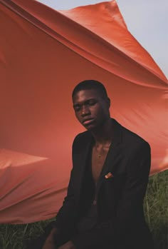 a man sitting in the grass with an orange umbrella behind him