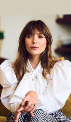 a woman sitting on top of a couch wearing a white shirt and checkered pants